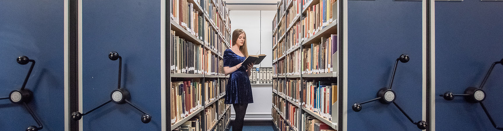 Bookshelves in the Leopold Muller Memorial Library A student holding a book between two bookshelves