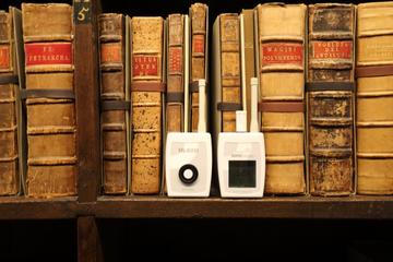 Two small white plastic monitors - for temperature and humidity - sit on a bookshelf in front of some rare books